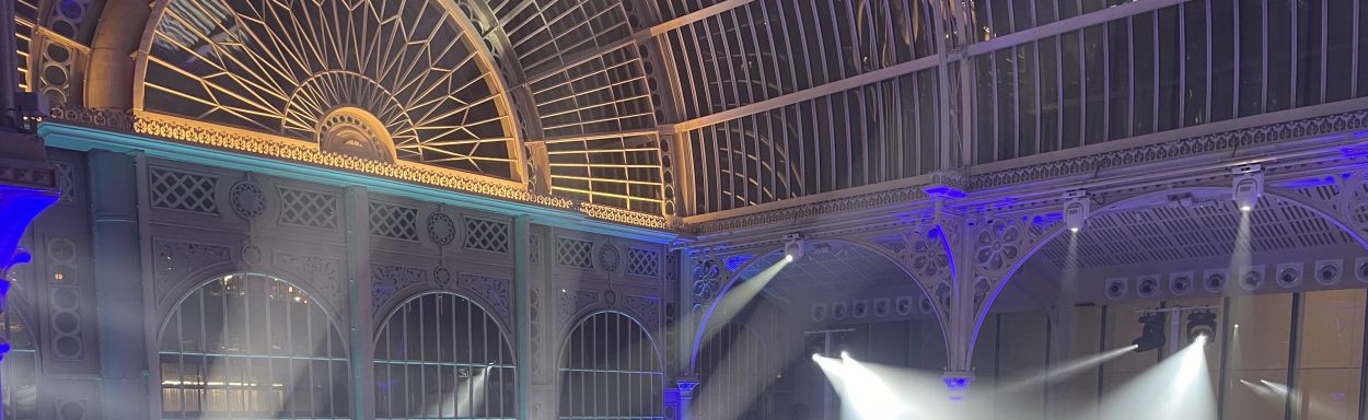 Nighttime view of a Victorian arched metal and glass roof lit for a elaborate event.
